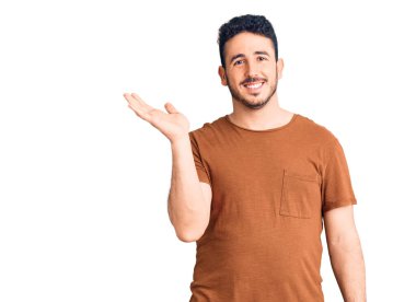 Gündelik kıyafetler giyen genç İspanyol adam neşeli bir şekilde gülümsüyor ve avuç içi kameraya bakıyor.. 