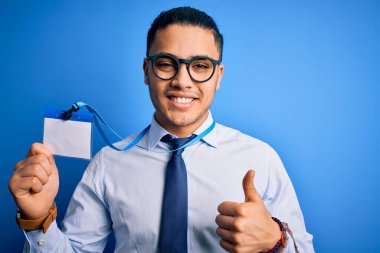 Genç Brezilyalı çağrı merkezi ajanı elinde kimlik kartı tutuyor. Kulaklık takıyor, gülümsüyor ve gülümsüyor. İşaret veriyor.