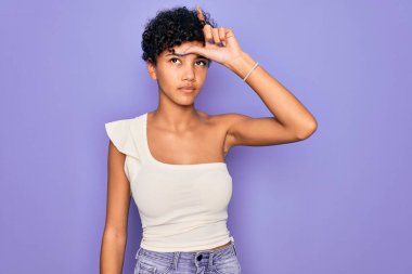 Genç ve güzel Afro-Amerikan kadın mor arka plan üzerine gündelik tişört giyiyor. Alnında parmakları olan insanlarla dalga geçiyor. Ezik jestler yapıyor, alay ediyor ve hakaret ediyor..