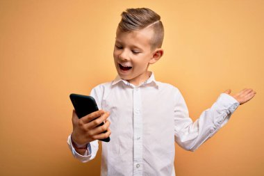 Küçük beyaz bir çocuk akıllı telefon kullanıyor. Telefona bakıyor. Çok mutlu ve heyecanlı. Kazanan ifade zaferi büyük bir gülümsemeyle kutluyor ve ellerini kaldırıyor.