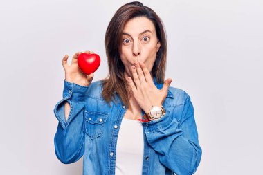 Doktor üniforması giyen genç ve güzel bir kadın kalbi elinde tutarak ağzı eliyle kapatıyor, şok geçiriyor ve hata yapmaktan korkuyor. şaşırmış ifade 