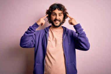 Genç, yakışıklı, sakallı, pembe arka planda rahat bir eşofman giyen, başını iki eliyle gösteren, harika bir fikir ya da düşünce, iyi bir hafıza.