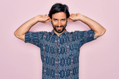 Pembe arka planda hippi tarzı giyinmiş genç, yakışıklı bohem bir adam parmaklarıyla kulaklarını çekerek gülüyor, komik bir jest. Seçme sorunu