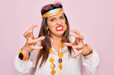 Genç İspanyol hippi kadın. Moda tarzı boho tarzı ve pembe arka planda güneş gözlüğü takıyor. Öfkeden köpürüyor, elleri boğmaya çalışıyor, deli gibi bağırıyor.