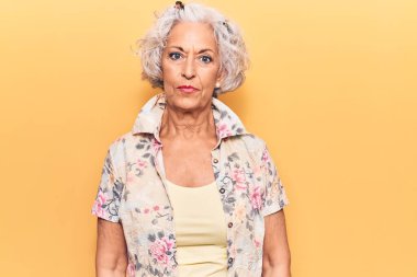 Yaşlı, gri saçlı, sıradan kıyafetler giyen, yüzünde ciddi bir ifade olan bir kadın. Basit ve doğal bir şekilde kameraya bakıyorsun.. 