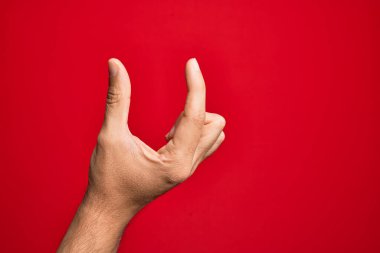 Kafkasyalı genç adam parmaklarını izole edilmiş kırmızı arka plan üzerinde gösteriyor ve görünmez şeyi alıyor, parmakları boşluk gösteren nesneleri tutuyor.