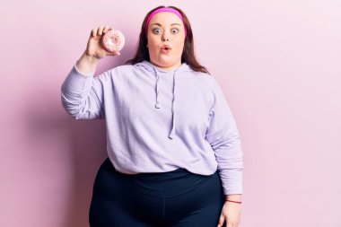 Genç ve cüsseli bir kadın elinde donut tutuyor. Korkmuş ve ağzı açık kalmış, şaşırmış ve şaşırmış. 