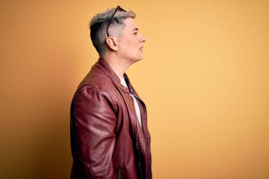 Sarı arka planda moda deri ceketi ve güneş gözlüğü takan yakışıklı, rahat bir görünüm takınan, kendine güvenen gülümseyen genç ve modern bir adam..