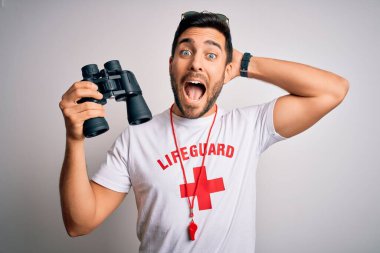 Sakallı, kırmızı haçlı ve güneş gözlüklü genç bir cankurtaran ıslık çalıyor ve elleriyle kafasından korkuyor, ağzı açık şok geçirmekten korkuyor ve şaşırıyor.