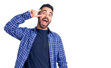 Gündelik kıyafetler giyen genç İspanyol adam barış sembolü yapıyor. Yüzünde parmaklar, gülümseyerek zaferi gösteriyor. 