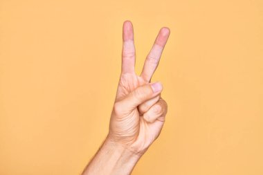 Kafkas genci parmaklarını izole edilmiş sarı arka planda gösteriyor. 2 numara iki parmağını gösteriyor, zafer işareti ve kazanan sembol.