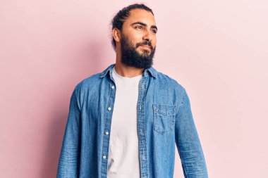 Gündelik giysiler giyen genç bir Arap, rahat bir görünüm takınıyor, doğal bir yüz ve kendine güvenen bir gülümsemeyle poz veriyor.. 