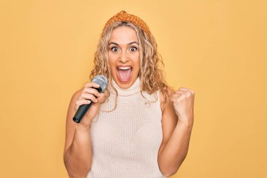 Sarışın, güzel bir şarkıcı. Sarı arka planda mikrofon kullanarak şarkı söylüyor. Gururla bağırıyor, zaferi kutluyor ve kollarını kaldırarak başarıyı kutluyor.