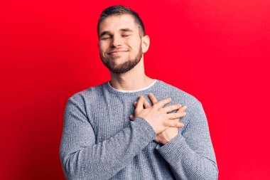 Elleri göğsünde gülümseyen sıradan bir süveter giyen genç yakışıklı bir adam. Minnettar bir yüz ifadesiyle gözleri kapalı. sağlık kavramı. 