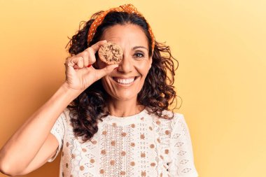 Orta yaşlı güzel bir kadın çikolatalı kurabiyeyi gözünün üstünde tutuyor. Olumlu ve mutlu görünüyor. Kendine güvenen bir gülümsemeyle dişlerini gösteriyor. 
