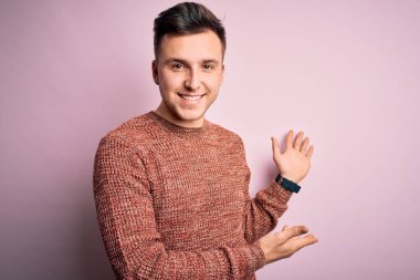 Pembe izole edilmiş arka plan üzerine sıradan bir kazak giyen yakışıklı beyaz adam gülümseyerek içeri girmeye davet ediyor.