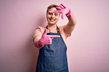 Genç, kızıl saçlı temizlikçi, önlük ve eldivenlerle ev işi yapıyor. Gülümsüyor, elleriyle ve parmaklarıyla mutlu bir yüz çiziyor. Yaratıcılık ve fotoğrafçılık kavramı.