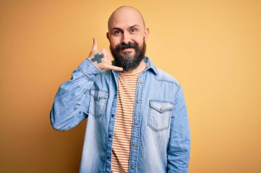 Sakallı, sıradan bir kot ceket ve çizgili tişört giyen, telefonla el ve parmak hareketleriyle gülümseyen, telefonda konuşan yakışıklı kel adam. İletişim kavramları.