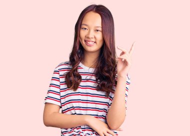 Genç, güzel, sıradan kıyafetler giyen, mutlu gülümseyen, el ve parmak uçlarında gezen Çinli bir kız. 