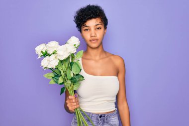 Güzel Afro-Amerikan Afro kadın elinde bir buket beyaz çiçekle mor arka planda, akıllı yüzünde kendine güvenen bir ifadeyle ciddi bir şekilde