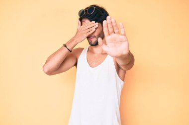Yaz bakışı takan yakışıklı İspanyol adam ve ellerle gözlerini kapayan güneş gözlüğü takan ve üzgün ve korku ifadeli jestler yapan. utangaç ve olumsuz kavram. 