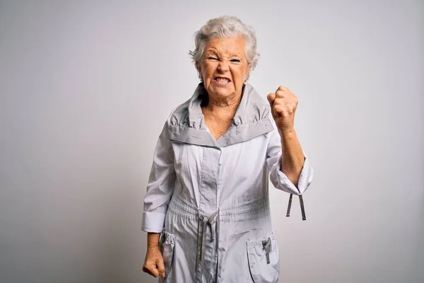Senior beautiful grey-haired woman wearing casual jacket standing over white background angry and mad raising fist frustrated and furious while shouting with anger. Rage and aggressive concept.