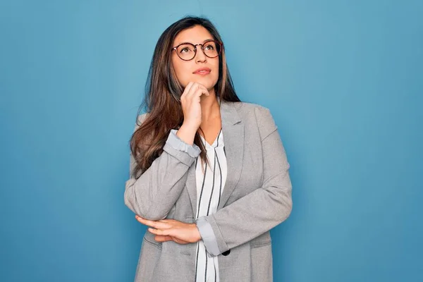 若いヒスパニック系のビジネス女性の質問については 集中的な表現を考えて顎に手で青の孤立した背景の上に立って眼鏡をかけて 笑顔と思慮深い顔 疑いの概念 — ストック写真