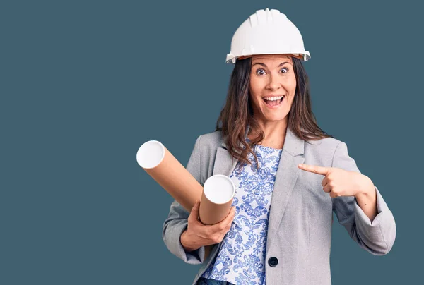 Jovem Bela Mulher Morena Vestindo Arquiteto Hardhat Segurando Blueprint Sorrindo — Fotografia de Stock