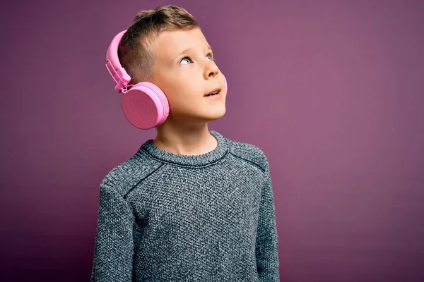 若い白人の子供は 紫色の背景の上に音楽を聞いてヘッドフォンを着用し 顔に笑みを浮かべて横に見て 自然な表現 自信を持って — ストック写真