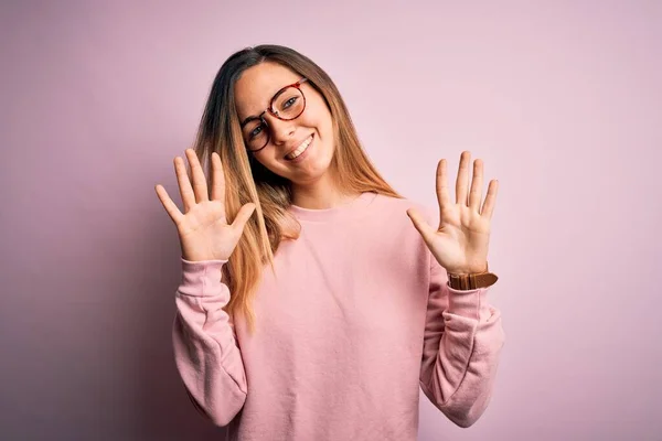 漂亮的金发女人 蓝眼睛 身穿毛衣 戴着眼镜 背景是粉色的 露出十号手指 面带微笑 自信而快乐 — 图库照片