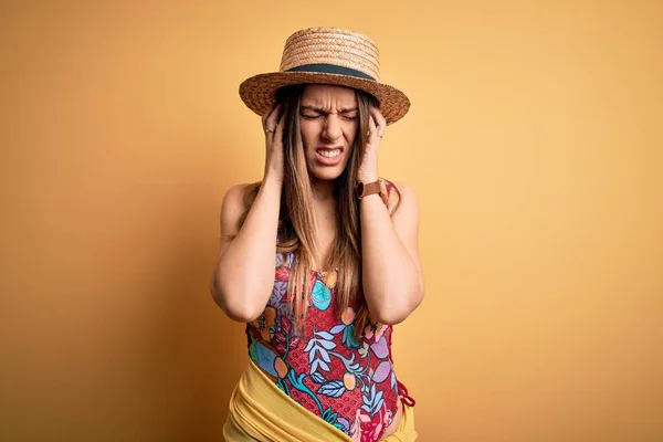 Young beautiful blonde woman wearing swimsuit and summer hat over yellow background suffering from headache desperate and stressed because pain and migraine. Hands on head.