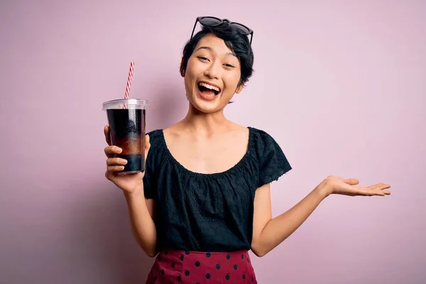 年轻美丽的中国女子 喝着红葡萄酒 背景粉红 喝着红葡萄酒 非常高兴 喜形于色 喜庆胜利 笑着举手表决胜利 — 图库照片