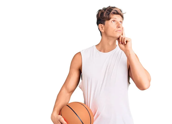 年轻英俊的男子拿着篮球 严肃的面庞 手托着下巴思考着问题 沉思着困惑的想法 — 图库照片