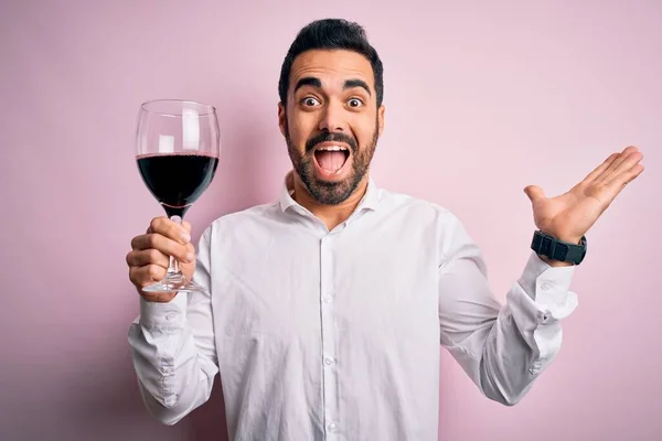 孤立したピンクの背景に赤ワインのひげを飲む若いハンサムな男は非常に幸せと興奮 大きな笑顔で叫んで勝利を祝う勝者式と手を上げ — ストック写真