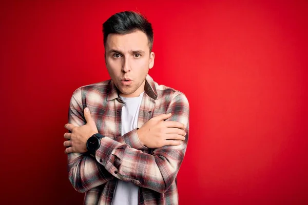 Young handsome caucasian man wearing casual modern shirt over red isolated background shaking and freezing for winter cold with sad and shock expression on face