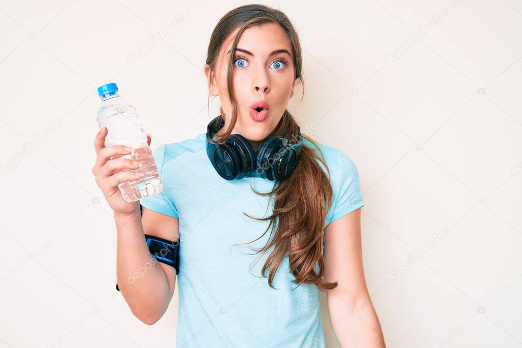 Beautiful young caucasian woman wearing sportswear drinking bottle of water scared and amazed with open mouth for surprise, disbelief face 
