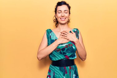 Genç ve güzel İspanyol bir kadın gündelik elbiseler giyiyor. Elleri göğsünde, gözleri kapalı gülümsüyor ve yüzünde minnet ifadesi var. sağlık kavramı. 