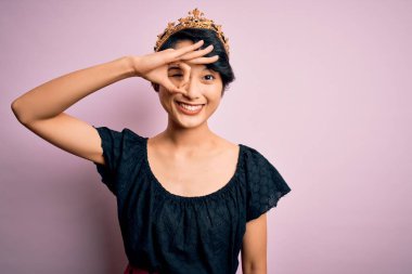 Genç, güzel Çinli kadın, kralın altın tacını takmış pembe arka planda el hareketleriyle gülümsüyor ve mutlu yüzüyle parmaklarının arasından bakıyor..