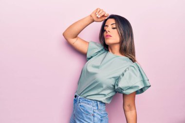 Genç, güzel, esmer, günlük kıyafetler giyen bir kadın izole edilmiş pembe arka planda dikiliyor.