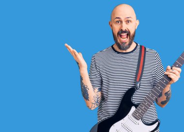 Genç yakışıklı adam zaferi kutlamak için elektro gitar çalıyor mutlu bir gülümseme ve kaldırılmış ellerle kazanan ifade. 