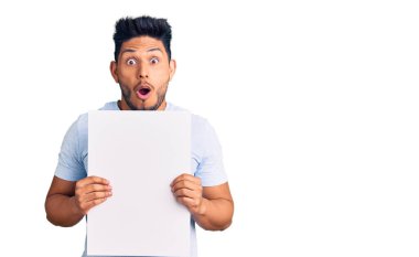 Yakışıklı Latin Amerikalı genç adam elinde boş alanı olan karton bir pankart tutuyor. Şaşırmak için ağzı açık kalmış, korkmuş ve şaşırmış. İnanmayan yüz. 