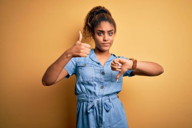 Sarı arka planda dikilen kot elbiseli güzel afro-amerikalı kız baş parmak kaldırıyor, anlaşmazlık ve uzlaşma ifadesi takınıyor. Çılgın çatışma