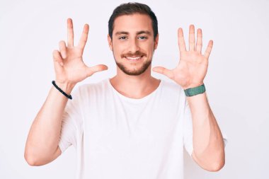 Gündelik beyaz tişört giyen genç yakışıklı adam 8 numaralı parmaklarını göstererek gülümseyerek kendinden emin ve mutlu görünüyor.. 