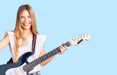 Sarışın, güzel, beyaz bir kadın. Elektro gitar çalıyor. Gururla bağırıyor, zaferi kutluyor ve kollarını kaldırarak başarıyı kutluyor. 