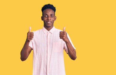 Genç afro-amerikan adam günlük kıyafetler giyiyor başarı işareti yapıyor, elleriyle olumlu jest yapıyor, gülümsüyor ve mutlu. Neşeli ifade ve kazanan jest. 