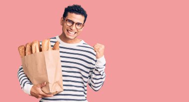 İspanyol asıllı yakışıklı genç adam elinde kağıt torbayla gururla bağırıyor zaferi kutluyor ve başarıyı kollarını kaldırarak kutluyor. 