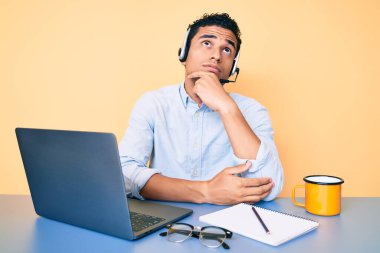 Genç, yakışıklı, ofiste çalışan, operatör kulaklığı takan, çenesinde parmak olan, şüpheye odaklanmış ve kafasını kaldırıp, 