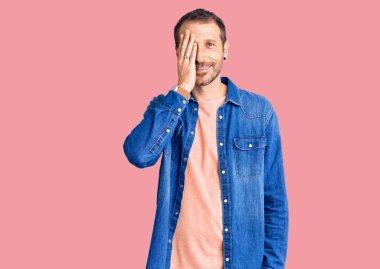 Gündelik kıyafetler giyen genç yakışıklı adam bir gözünü eliyle kapatıyor, yüzünde kendine güvenen bir gülümseme ve şaşırtıcı bir duygu var.. 