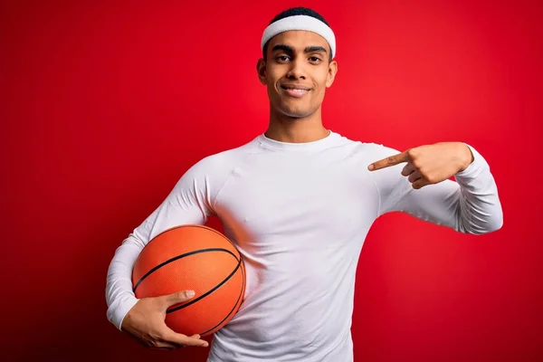 Junger Gutaussehender Afrikanisch Amerikanischer Sportler Hält Basketballball Über Rotem Hintergrund — Stockfoto