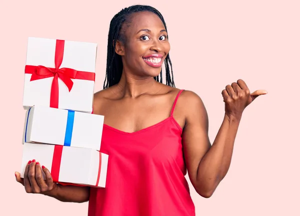 Joven Mujer Afroamericana Sosteniendo Regalo Señalando Pulgar Hacia Lado Sonriendo — Foto de Stock